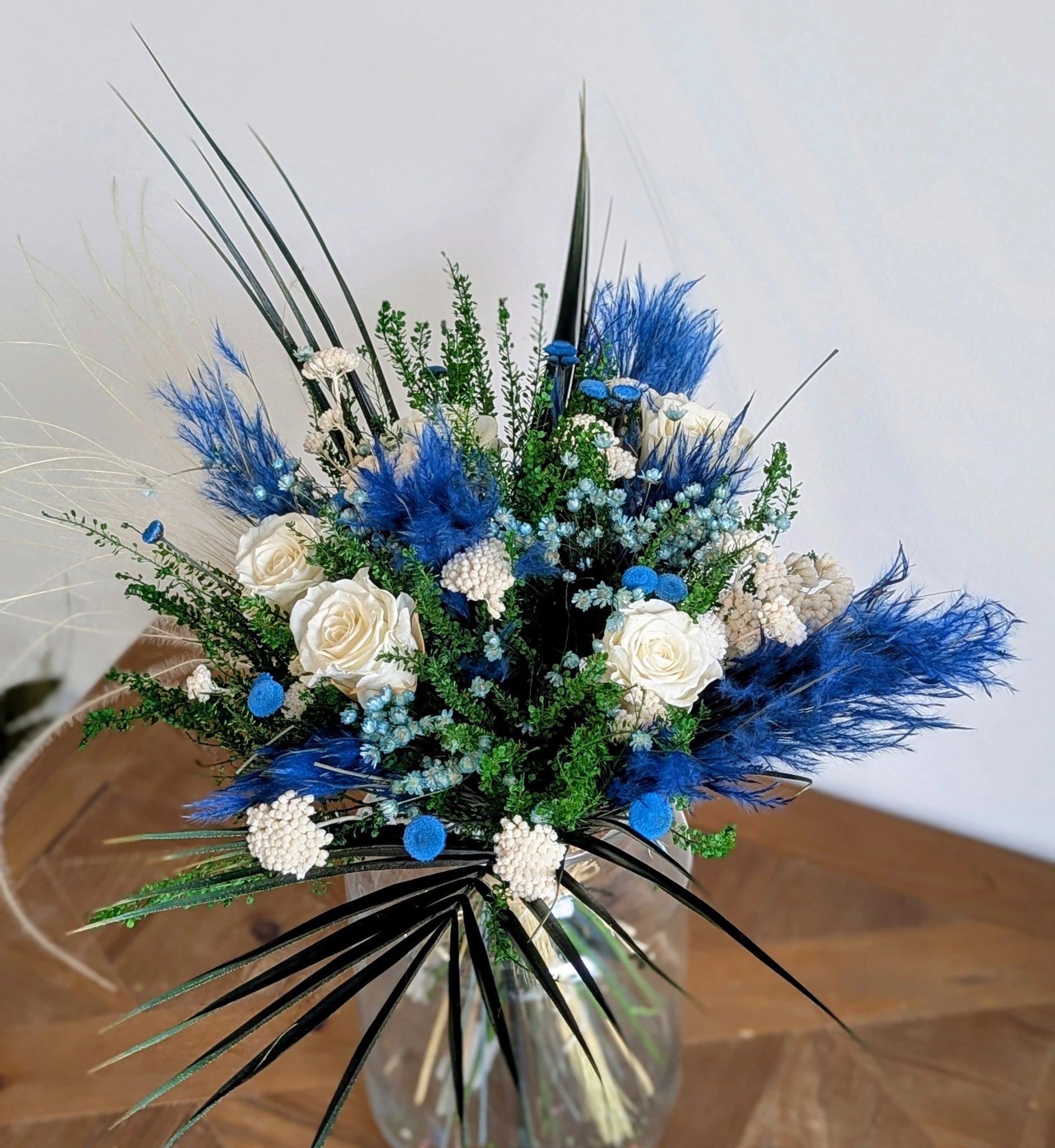 Bouquet AZUR avec roses ivoire et fleurs stabilisées bleu intense dans un vase transparent