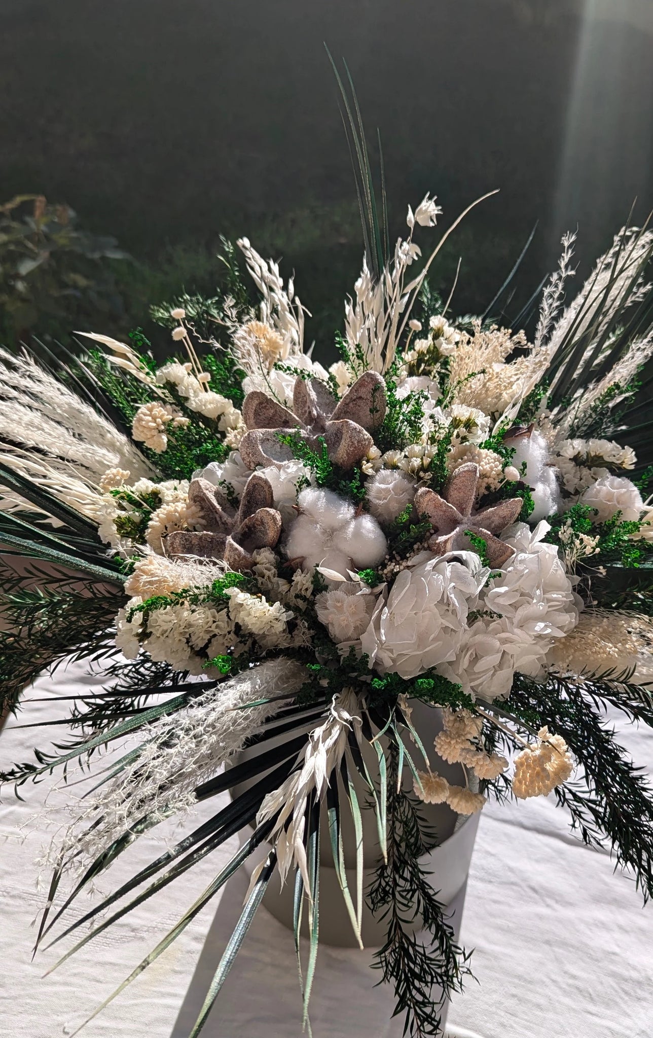 Composition en fleurs élégantes préservées mêlant achillée, coton, hortensias blancs et feuillages verts. Une création raffinée et durable, parfaite pour une ambiance hivernale et chaleureuse. Vase en métal vert  olive. A la lumière du jour