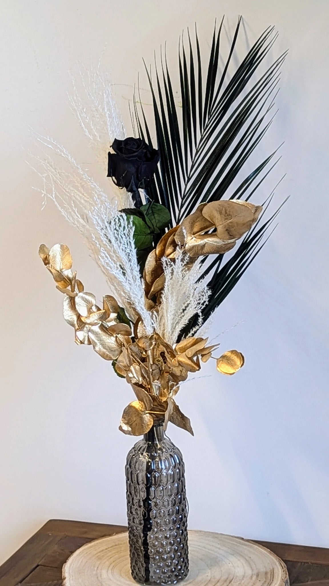 Élégance audacieuse en noir et or
Découvrez ce magnifique arrangement floral, un mariage harmonieux de raffinement et de modernité. Composé de fleurs préservées et séchées, cet ensemble unique associe la profondeur du noir avec des accents dorés étincelants, sublimés par des touches blanches et des textures végétales.
Présenté dans un élégant vase en verre texturé, il est parfait pour ajouter une touche sophistiquée à votre intérieur ou pour offrir en cadeau. SARAH AVEC VASE NOIR