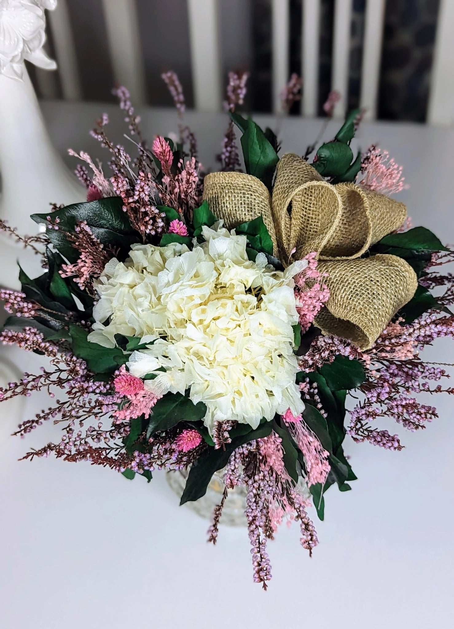 Blanc pur, rose tendre et un nœud en toile de jute : ce bouquet en fleurs stabilisées séduit par son charme naturel et sa durabilité. Une pièce idéale pour décorer ou célébrer un moment spécial avec délicatesse et raffinement.