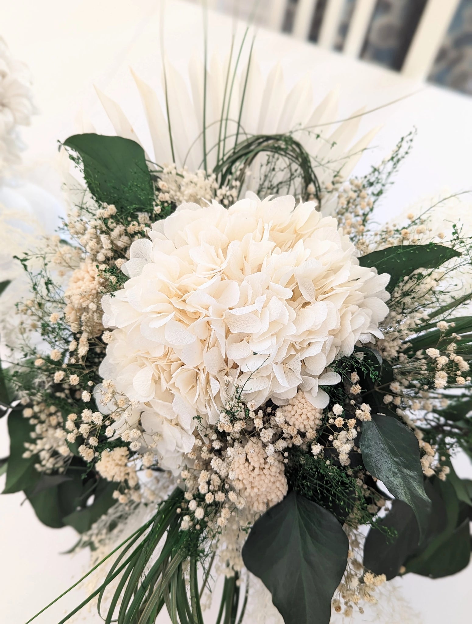 L'art floral éternel : Blanc éclatant et verdure vibrante s'unissent dans ce bouquet qui allie grâce et durabilité, pour embellir votre espace avec poésie. Blandine