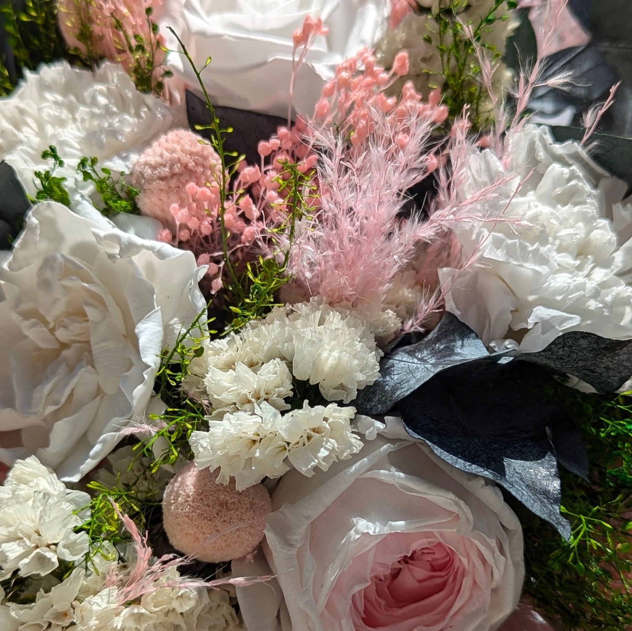 Douceur - Laissez-vous séduire par ce bouquet délicat où la douceur des roses poudrées s'entrelace avec la légèreté des pampas et l'éclat des fleurs blanches préservées. Une harmonie parfaite de textures et de couleurs, rehaussée par des touches végétales d'eucalyptus, pour une création à la fois poétique et durable. 🌿 Durabilité et beauté réunies, en gros plan