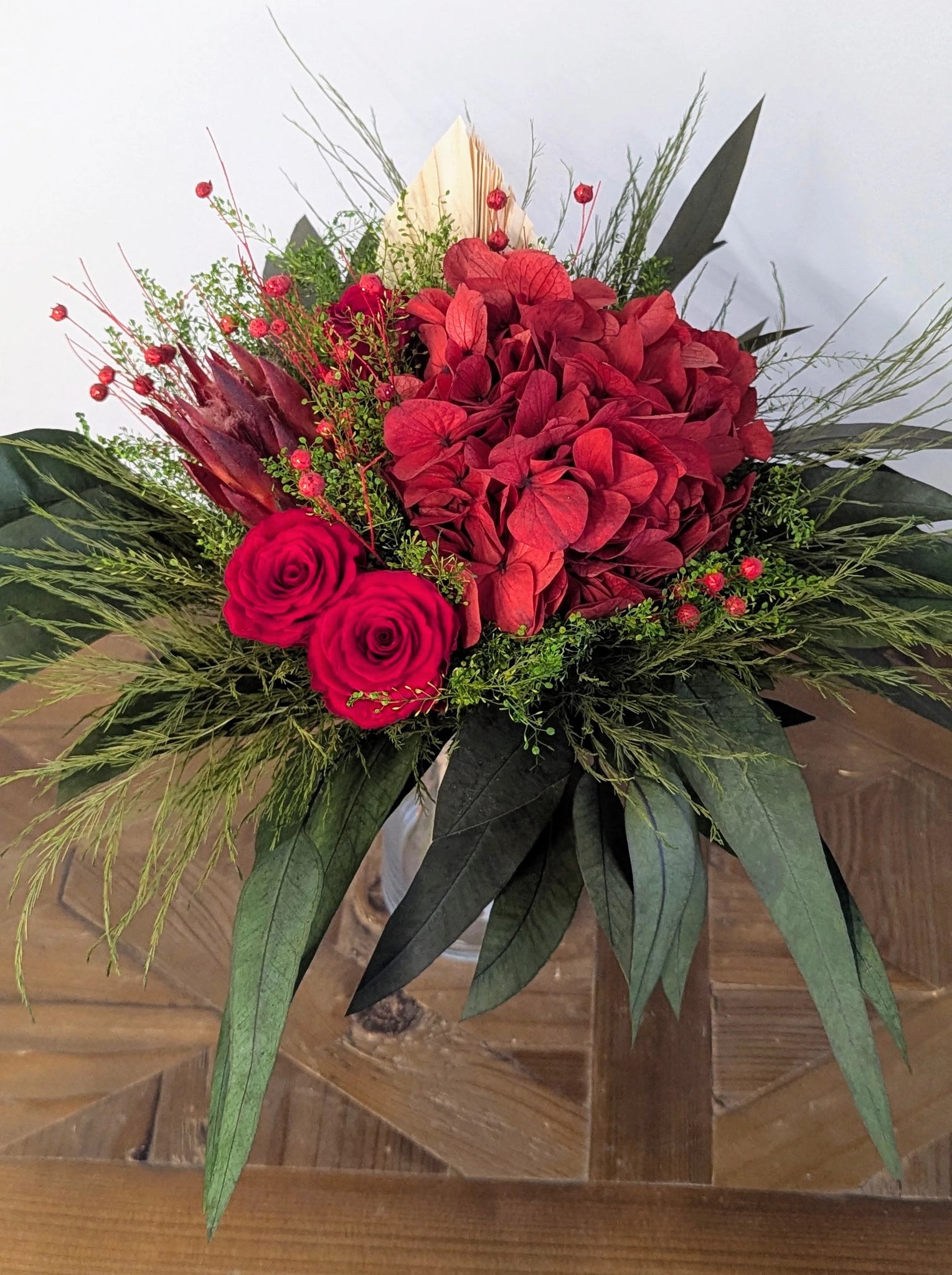 Alliance de matières naturelles et de fleurs stabilisées, ce bouquet offre une harmonie de rouges et de verts pour une décoration pleine de caractère… qui dure dans le temps.