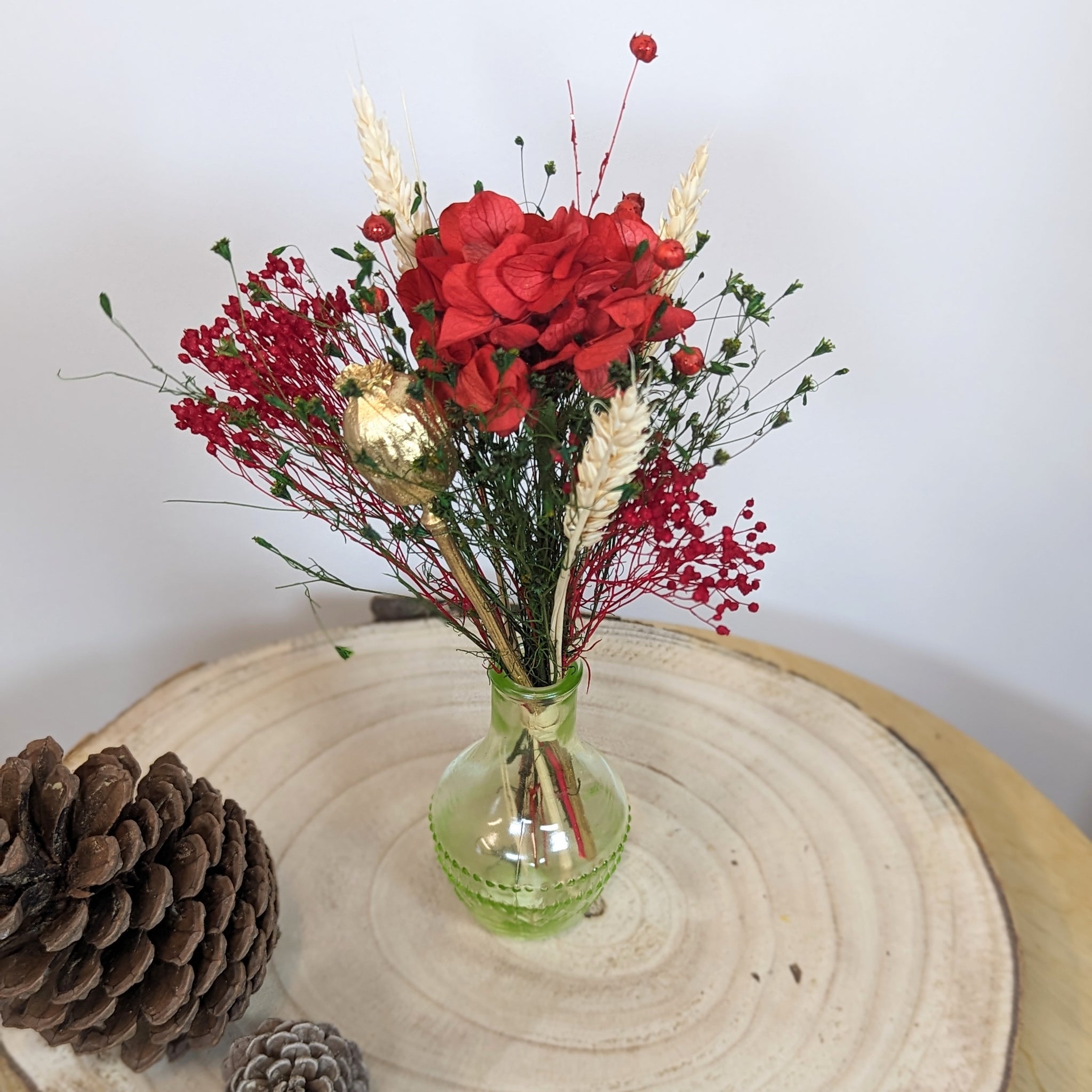 composition de fleurs rouges et fleurs séchées sur plateau bois et pigne de pin
